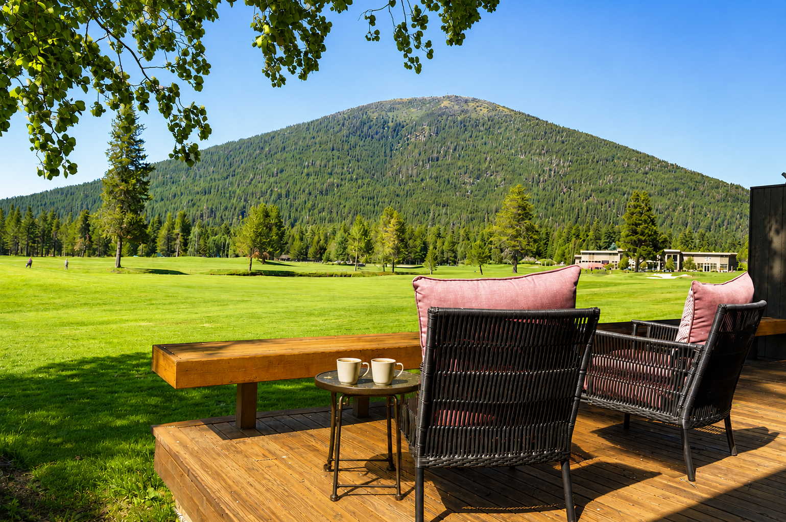 Expansive mountain views with forested slopes frame this serene outdoor setting, surrounded by open lawns and distant property buildings under clear blue skies.