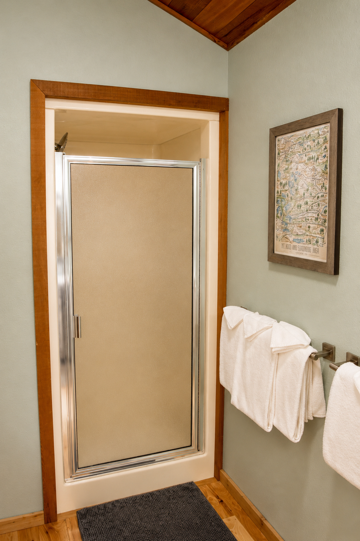 Step into your private en-suite bathroom with a spacious walk-in shower, complete with plush towels and warm wood accents for a cozy, home-like experience.