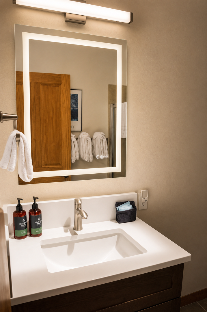 Your private bathroom features a modern vanity with premium amenities, LED-lit mirror, and plush towels—a serene space to refresh and unwind.