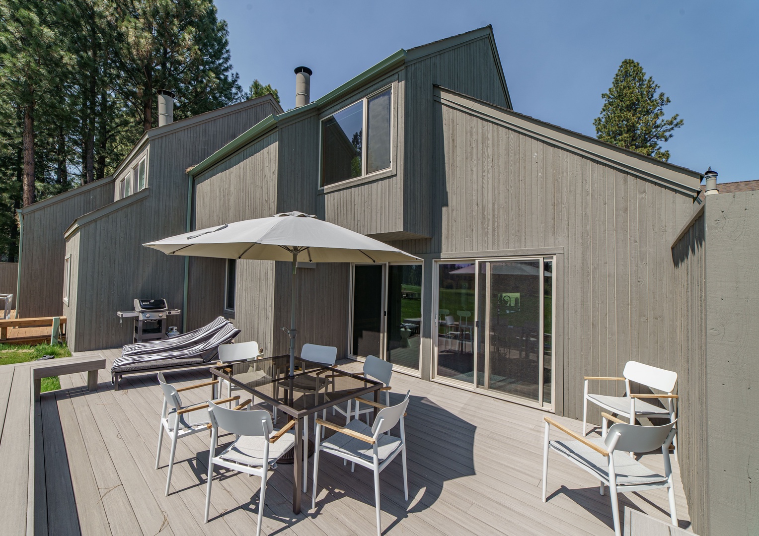 Modern vacation home with spacious deck and outdoor dining surrounded by towering pines.