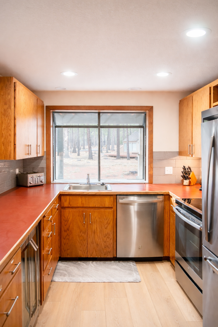 Cook with inspiring forest views through this modern kitchen's picture window, featuring warm wood cabinets and sleek stainless appliances.