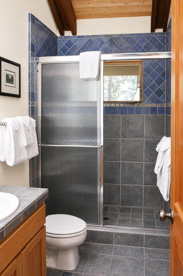 Step into your private bathroom featuring a walk-in shower with elegant blue tilework and warm wooden accents. Plush towels await you after a refreshing rinse.