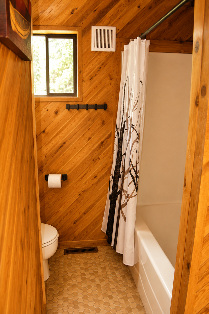 Cozy wood-paneled bathroom with a tub-shower combo, natural light from a window, and rustic touches like a branch shower curtain rod. Perfect for freshening up after your adventures.