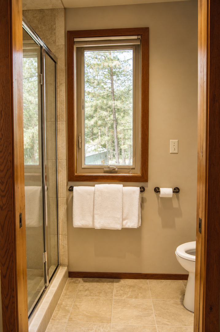 Your private bathroom features a refreshing shower and a peaceful forest view through the window, with plush towels awaiting you.