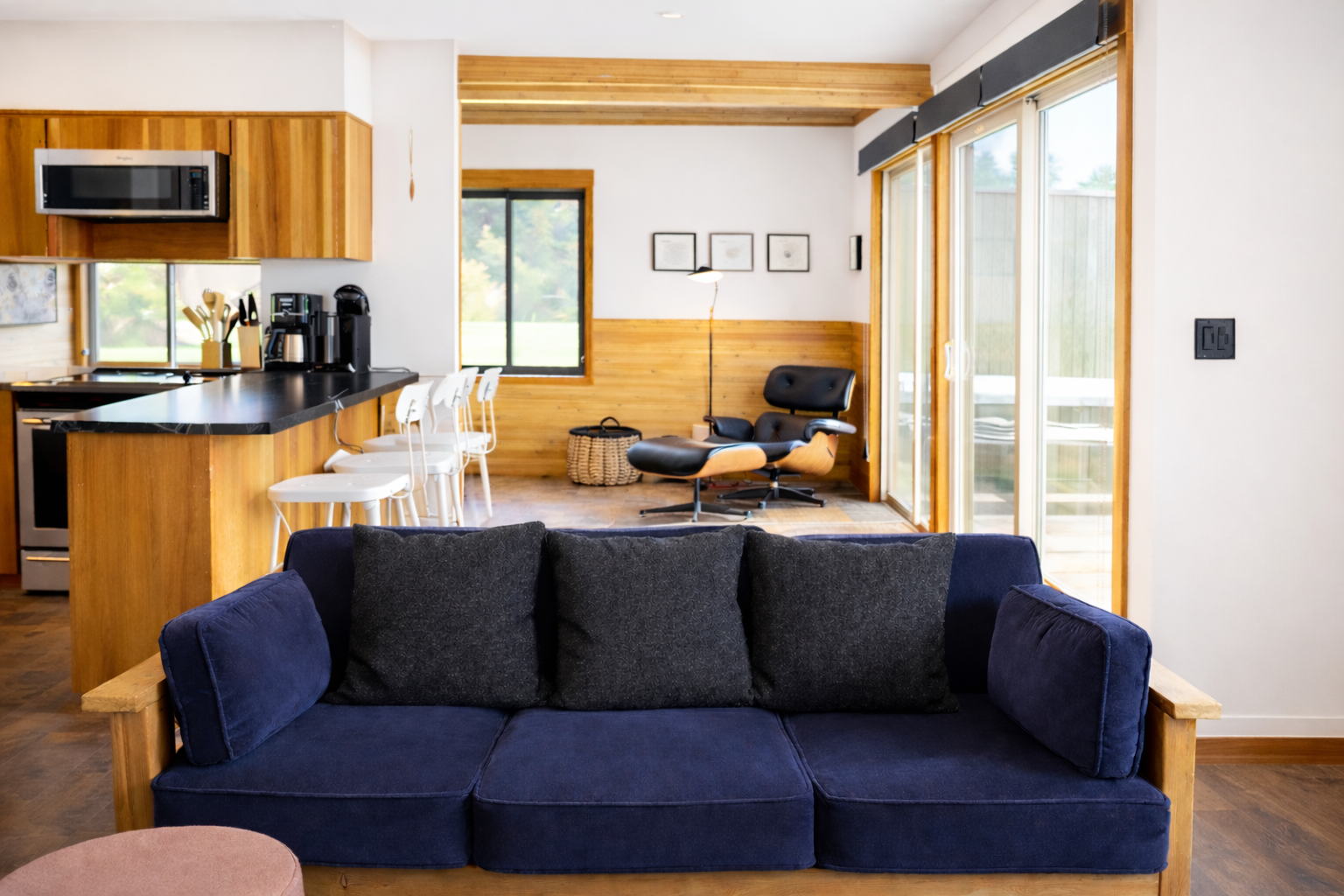 Sink into your comfortable blue sofa while taking in the open-concept design with warm wood accents and natural light streaming through floor-to-ceiling windows.