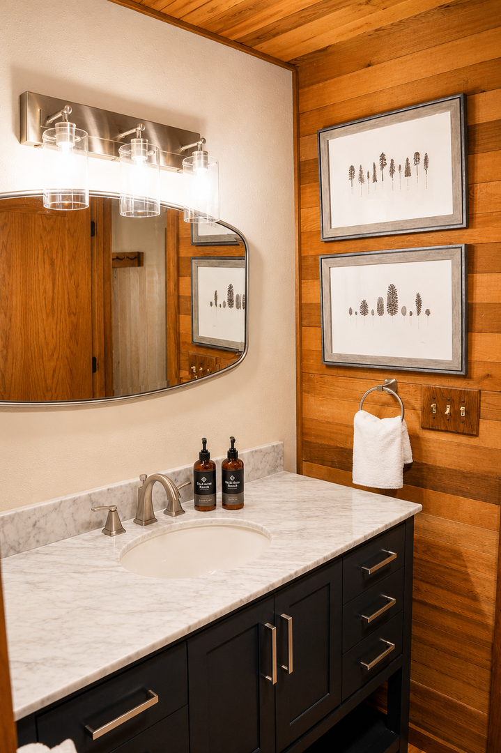 Step into your private bathroom featuring a polished marble vanity, warm wood-paneled walls, and nature-inspired artwork that brings a cozy, modern mountain retreat vibe to your stay.