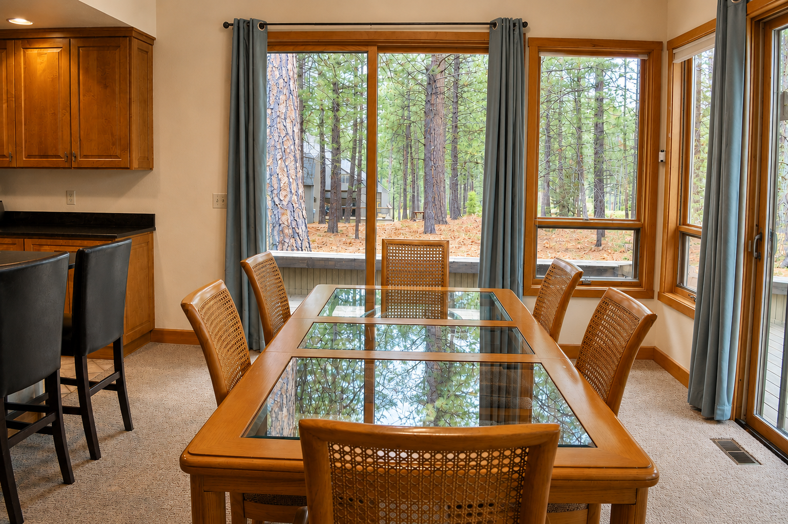 Gather around this inviting dining table where sunlight streams through floor-to-ceiling windows, framing serene forest views. You'll love sharing meals with nature as your backdrop in this warm, open space.