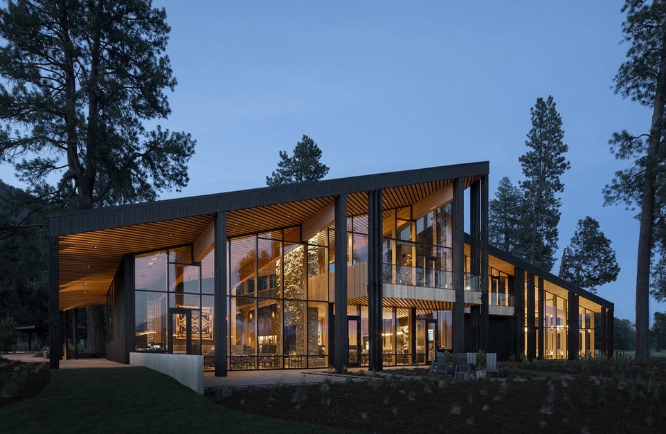 Stunning modern architecture nestled among towering trees with floor-to-ceiling windows showcasing warm interior lighting at dusk.
