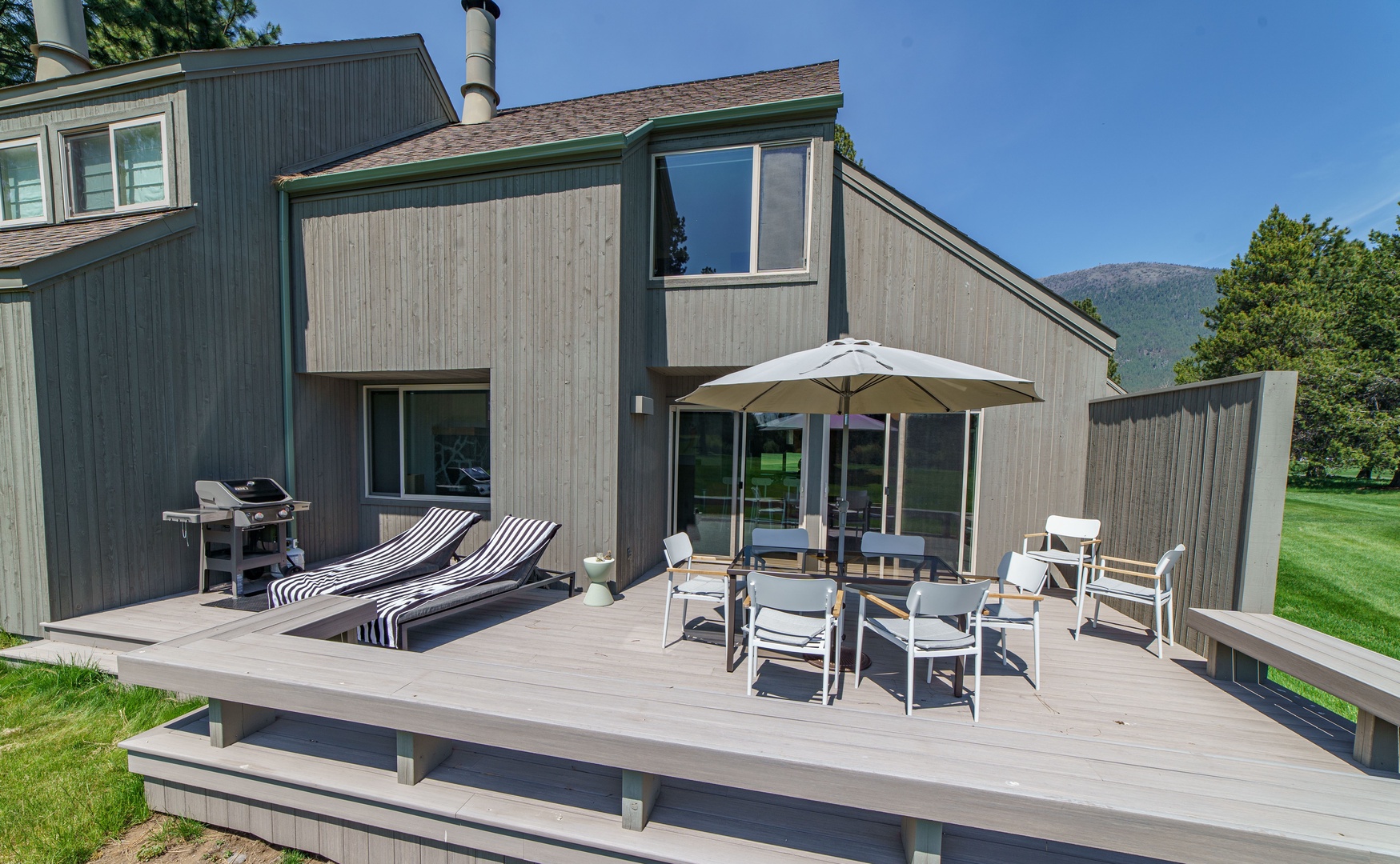 Modern vacation home features spacious deck with dining area, BBQ grill, and mountain backdrop for memorable outdoor gatherings.