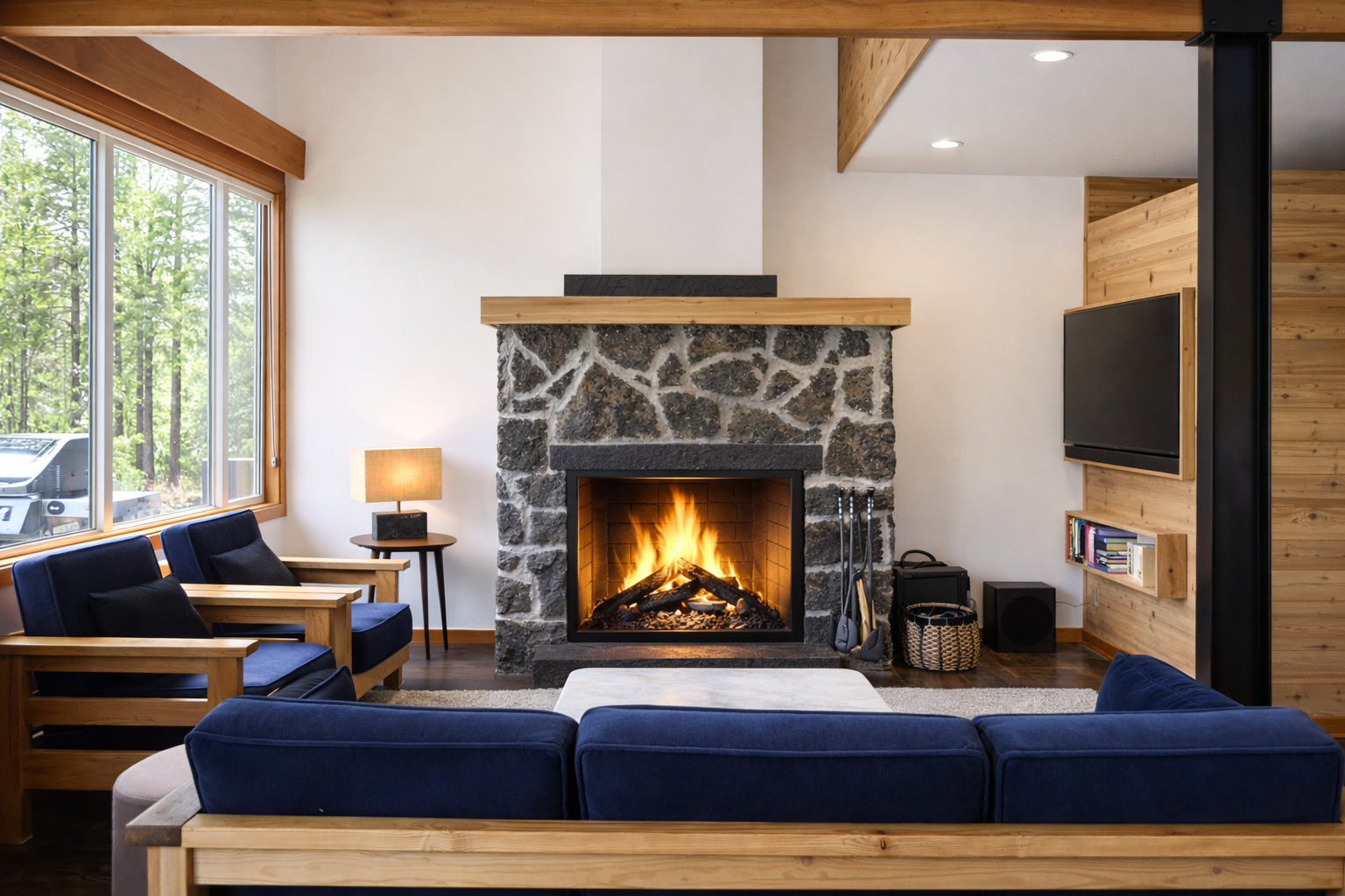 Unwind in your cozy living room where crackling flames dance in the stone fireplace, casting warm light across plush navy seating and natural wood beams.