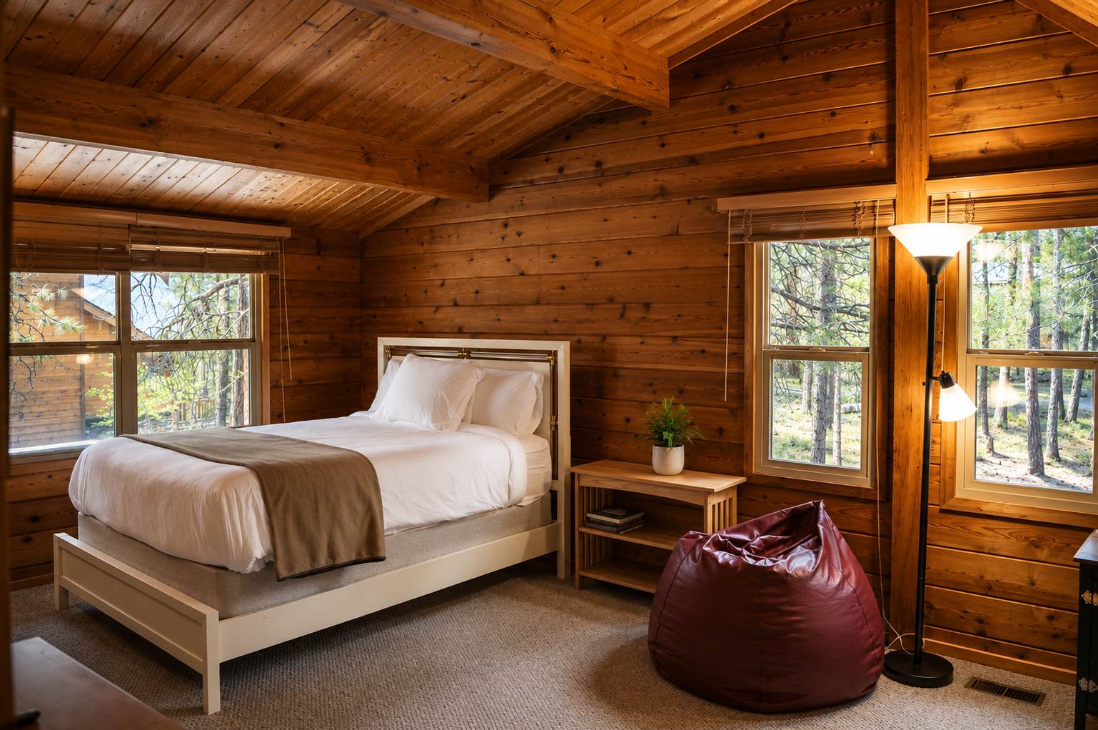 Unwind in your cozy cabin bedroom with warm wood walls and forest views framed by large windows. Sink into crisp linens, relax in the beanbag nook, and let nature's serenity surround you.