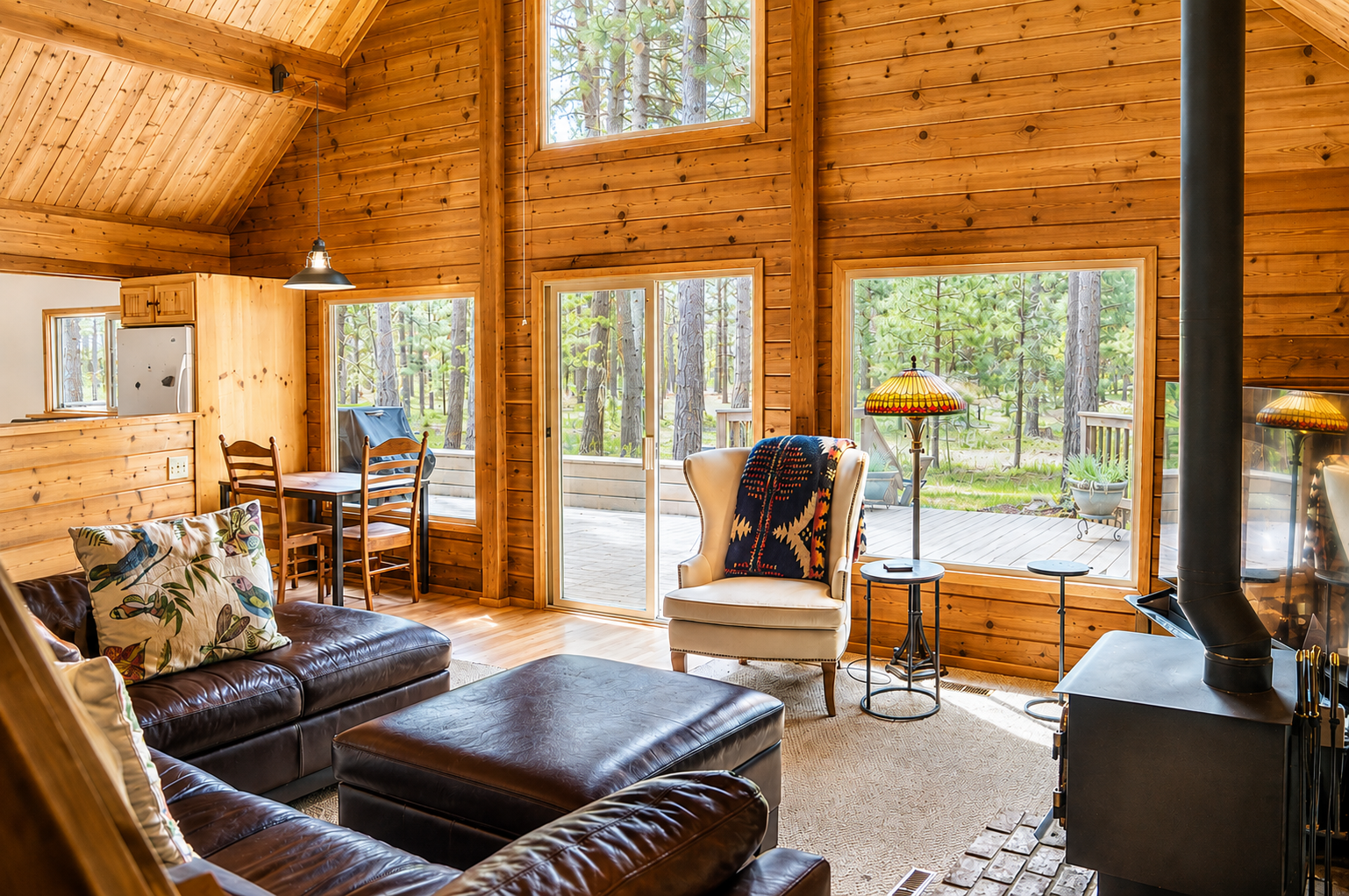 Relax in your cozy cabin living room surrounded by warm wood and towering windows that frame peaceful forest views, inviting natural light to fill your space.