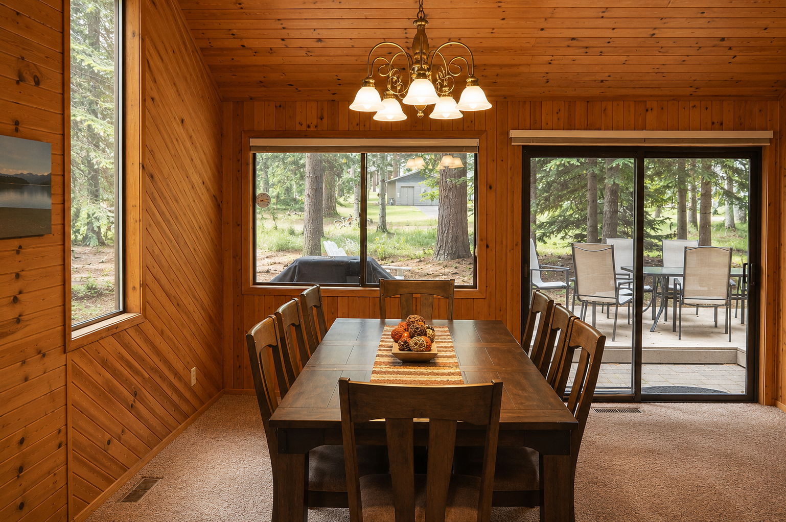 Gather around this warm wooden dining space where floor-to-ceiling windows invite nature inside. Step through glass doors to your private patio and enjoy peaceful forest views.