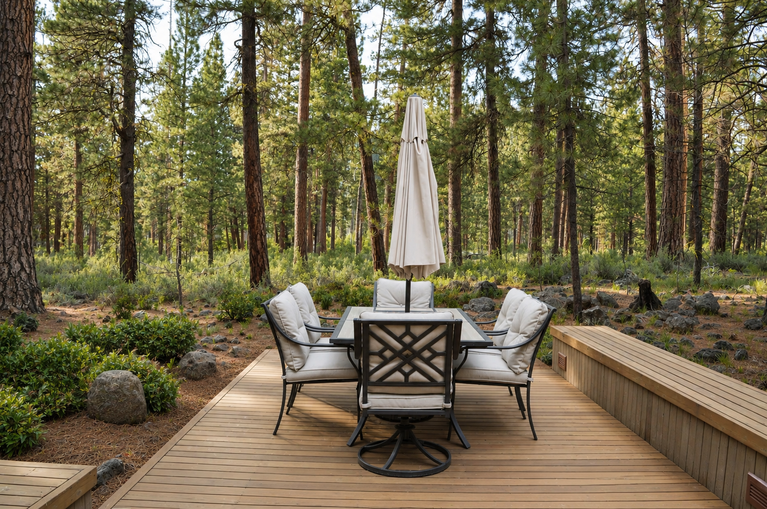 A private deck nestled among tall pines and natural forest. Features an outdoor dining table with umbrella and cushioned seating—ideal for morning coffee or evening gatherings surrounded by serene woodland views.