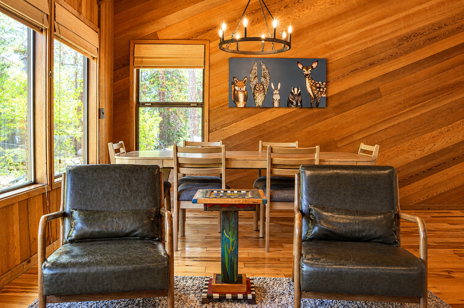 Settle into rich leather seating beneath warm wood beams, where a rustic chandelier casts a cozy glow. Your dining table overlooks forest views, inviting relaxed meals and game nights in this charming cabin retreat.
