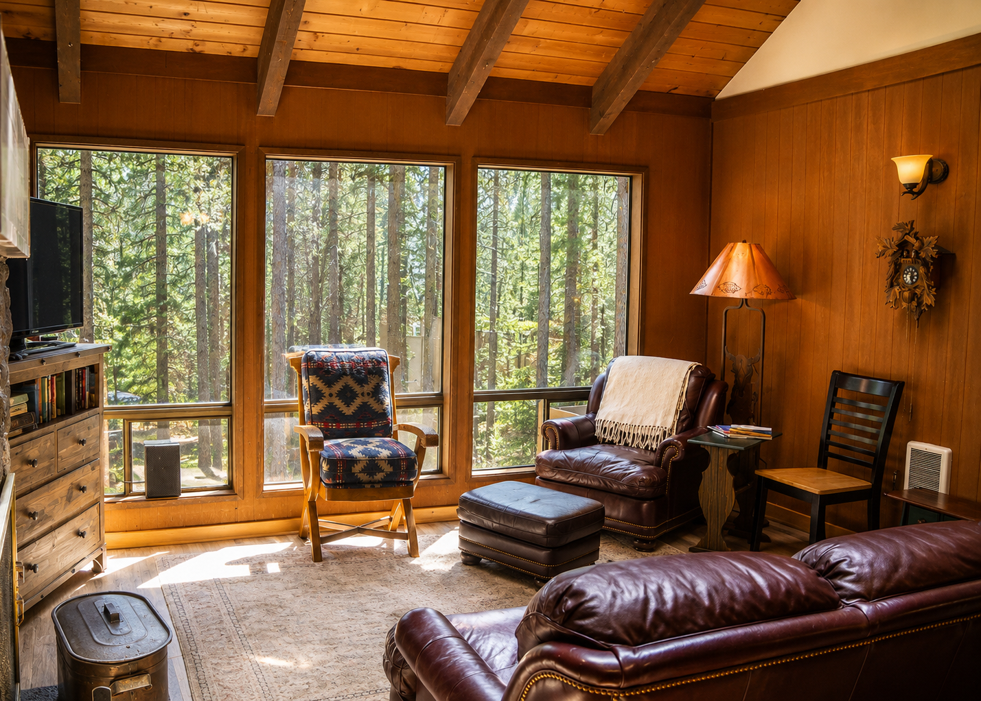 Sink into plush leather seating in your cozy living room, where towering pines frame floor-to-ceiling windows and warm wood beams cradle your mountain retreat.