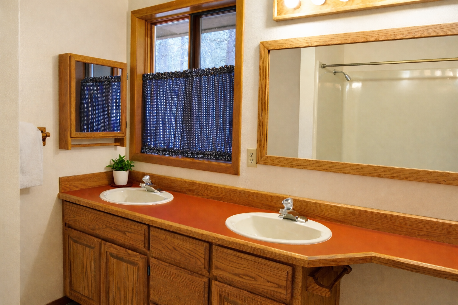 Freshen up at your spacious double vanity with warm wood cabinets and natural light from charming curtained windows.