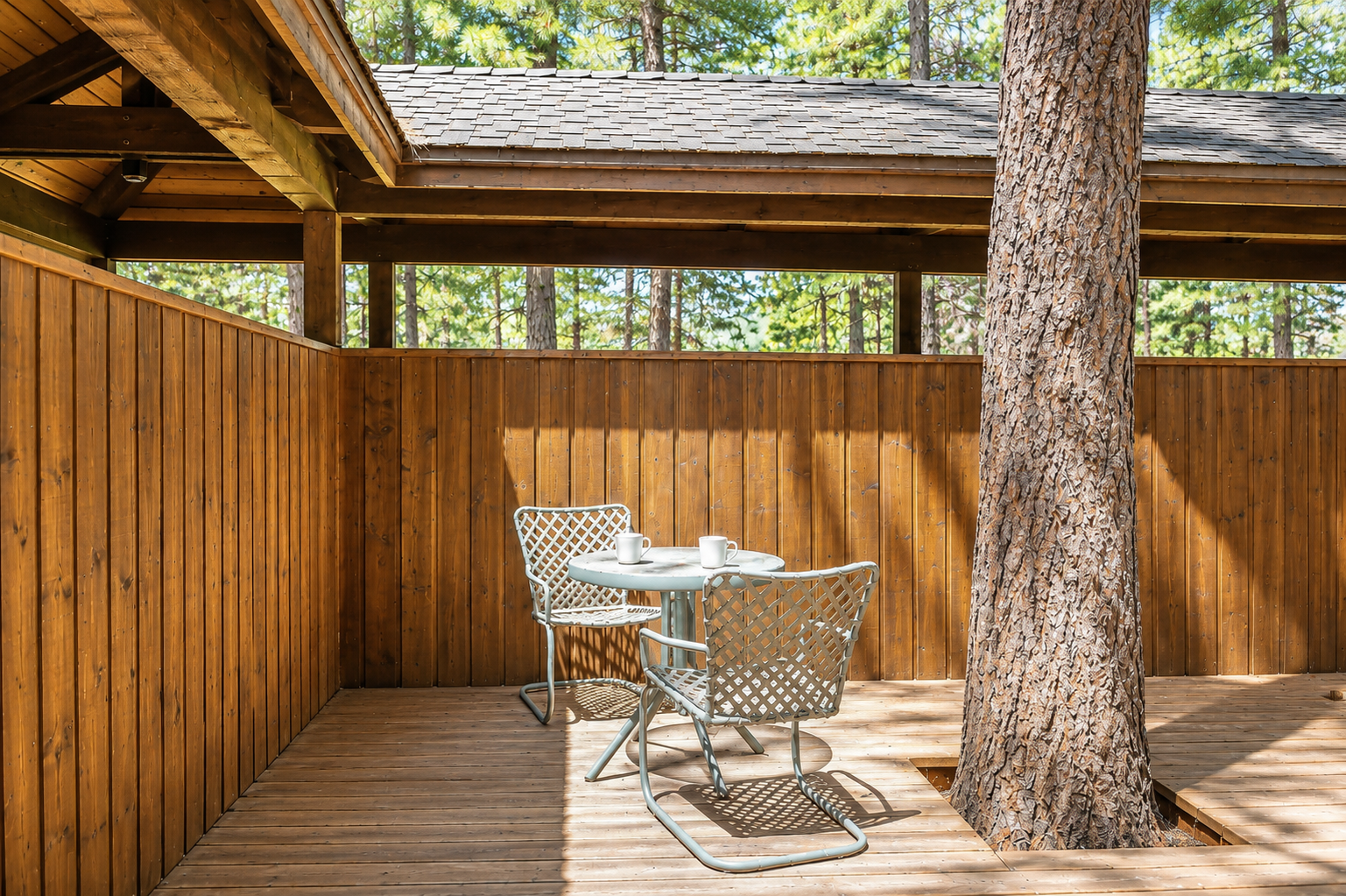 Covered deck with dining table nestled among towering pines, offering a peaceful spot for morning coffee or evening meals surrounded by forest beauty.