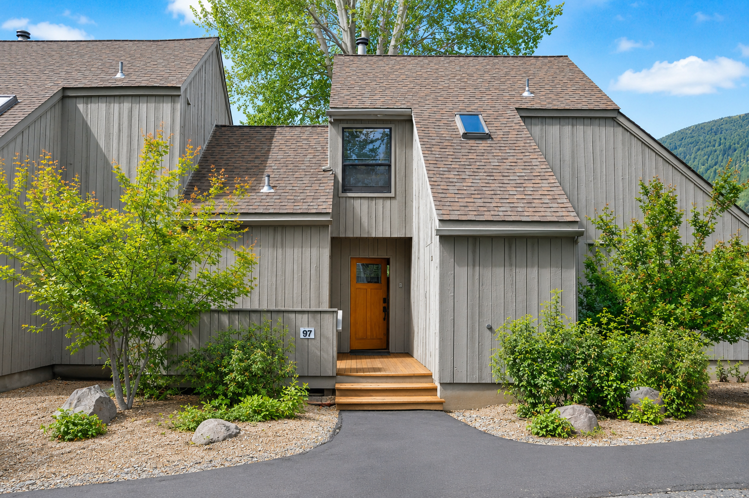 Modern mountain retreat with natural wood siding and welcoming entrance, nestled among lush greenery with scenic hillside backdrop.