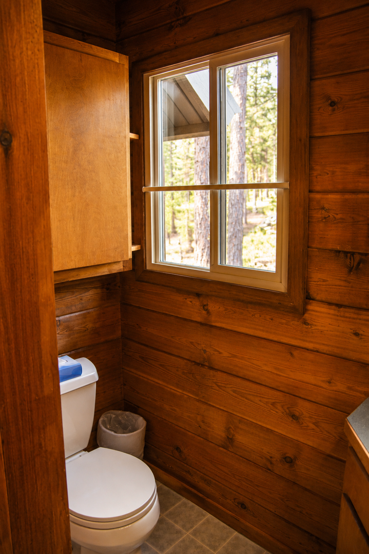 Warm wood panels surround your cozy bathroom, where natural light pours through the window, framing peaceful forest views that bring the outdoors in.
