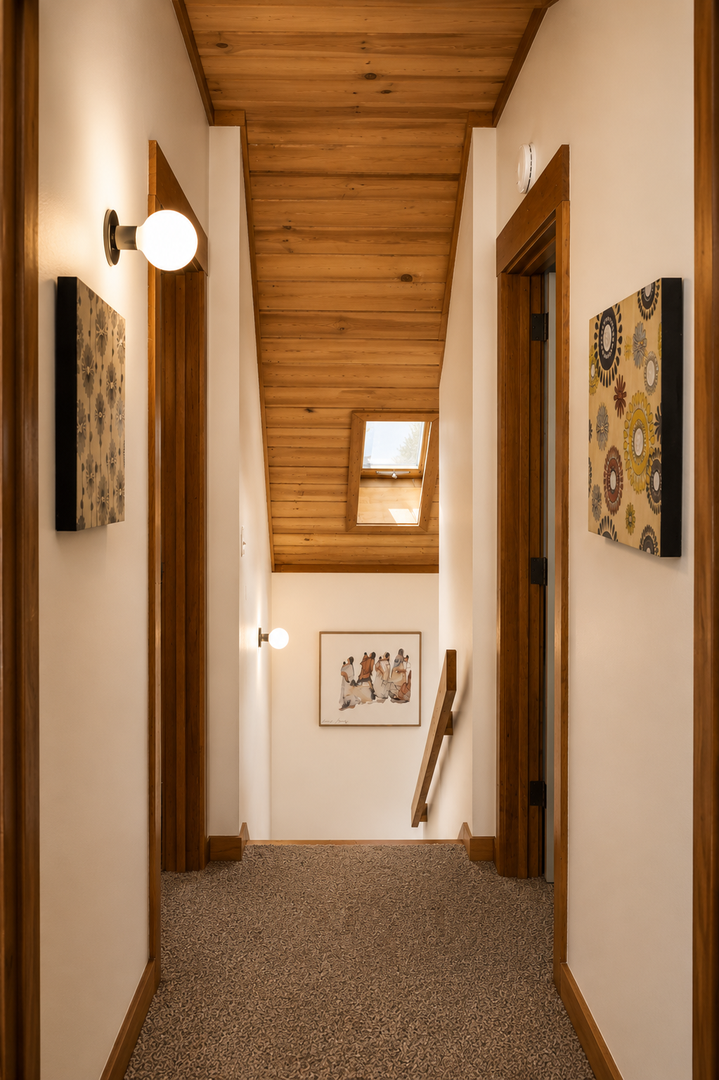 A welcoming hallway with warm wood accents, skylights, and curated artwork guides you to your private retreat with inviting natural light and comfortable carpeting.