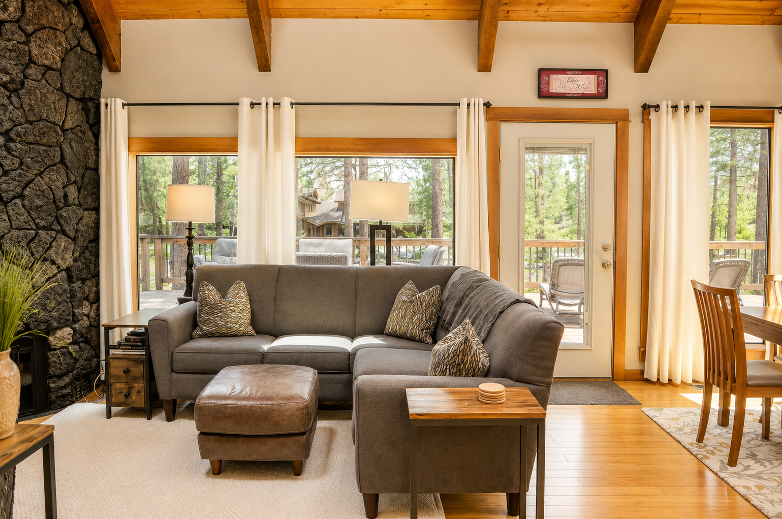 Settle into the inviting living room where natural light pours through expansive windows, revealing peaceful forest views. Your cozy sectional and vaulted wood-beam ceilings create the perfect retreat after mountain adventures.