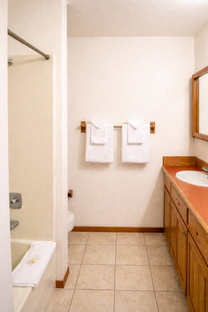 Your spacious bathroom features warm wood vanity, fresh towels, and tile floors for comfortable morning routines.
