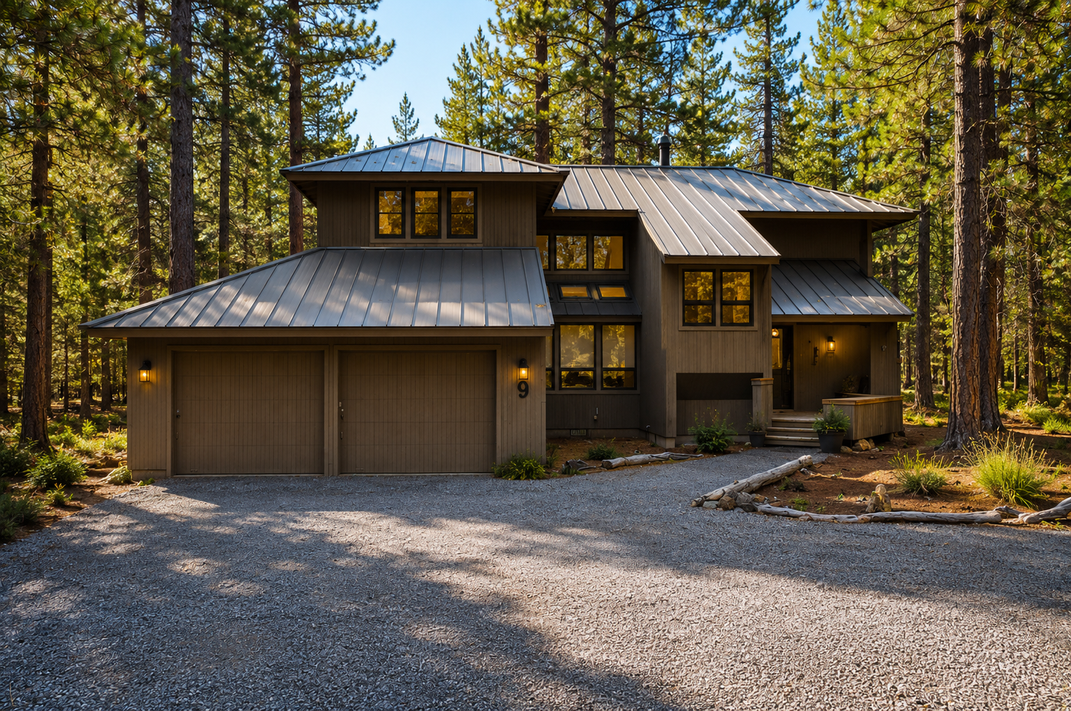 Modern mountain retreat nestled among towering pines, featuring spacious two-car garage and natural landscaping with convenient gravel driveway arrival.