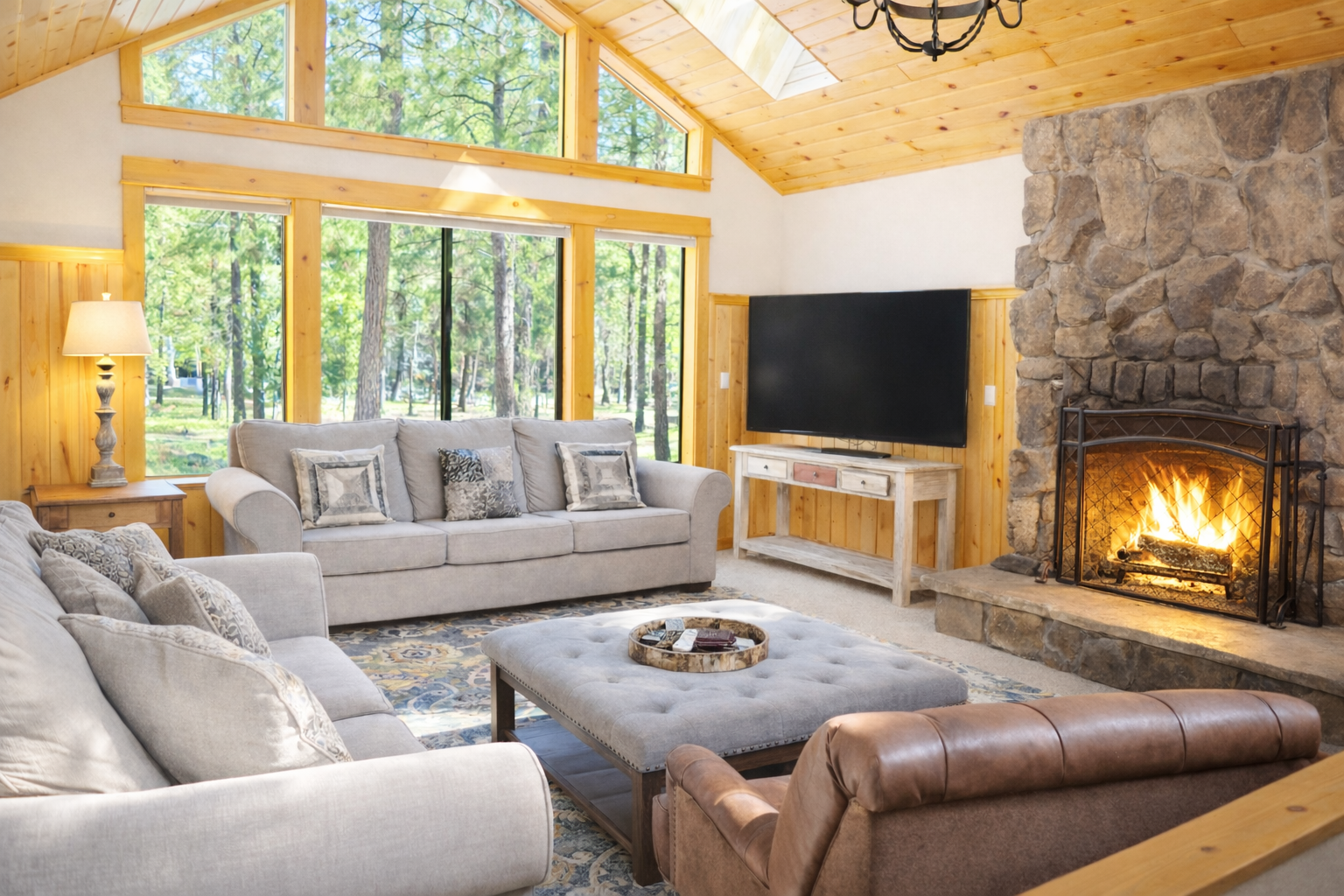 Cozy up by the crackling stone fireplace in this bright living room with forest views streaming through panoramic windows.