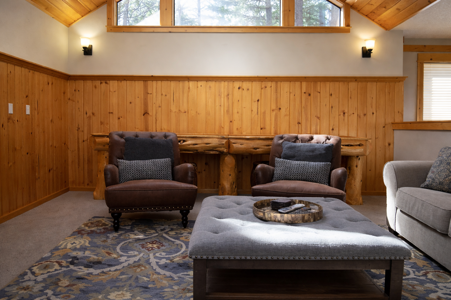 Sink into plush armchairs by the rustic stone fireplace, where warm wood paneling and cathedral windows create your perfect mountain retreat sanctuary.