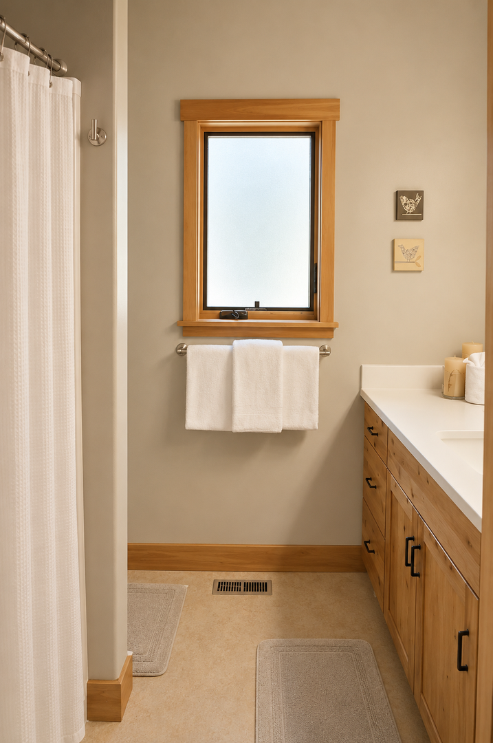 Step into your private bathroom, where warm wood tones and soft lighting create a serene escape. Fresh towels await beneath the sunlit window, and plush bath mats cushion your every step.