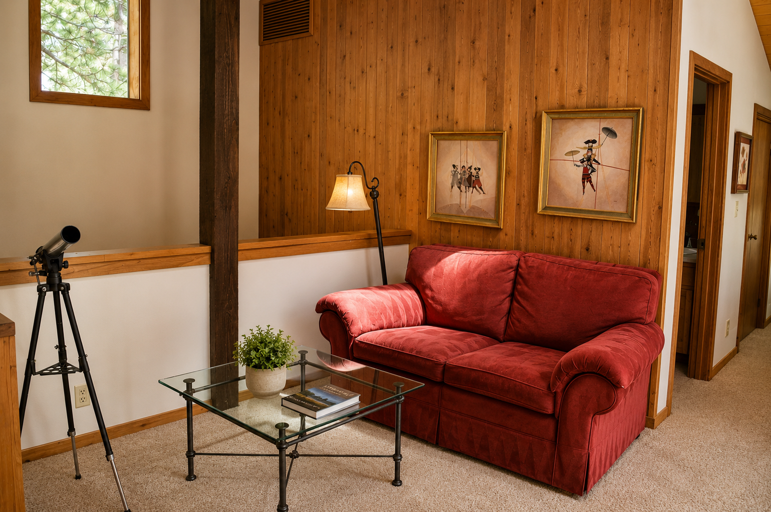 Unwind on the plush red sofa in your cozy living space, where warm wood paneling and charming art create a welcoming mountain retreat atmosphere.