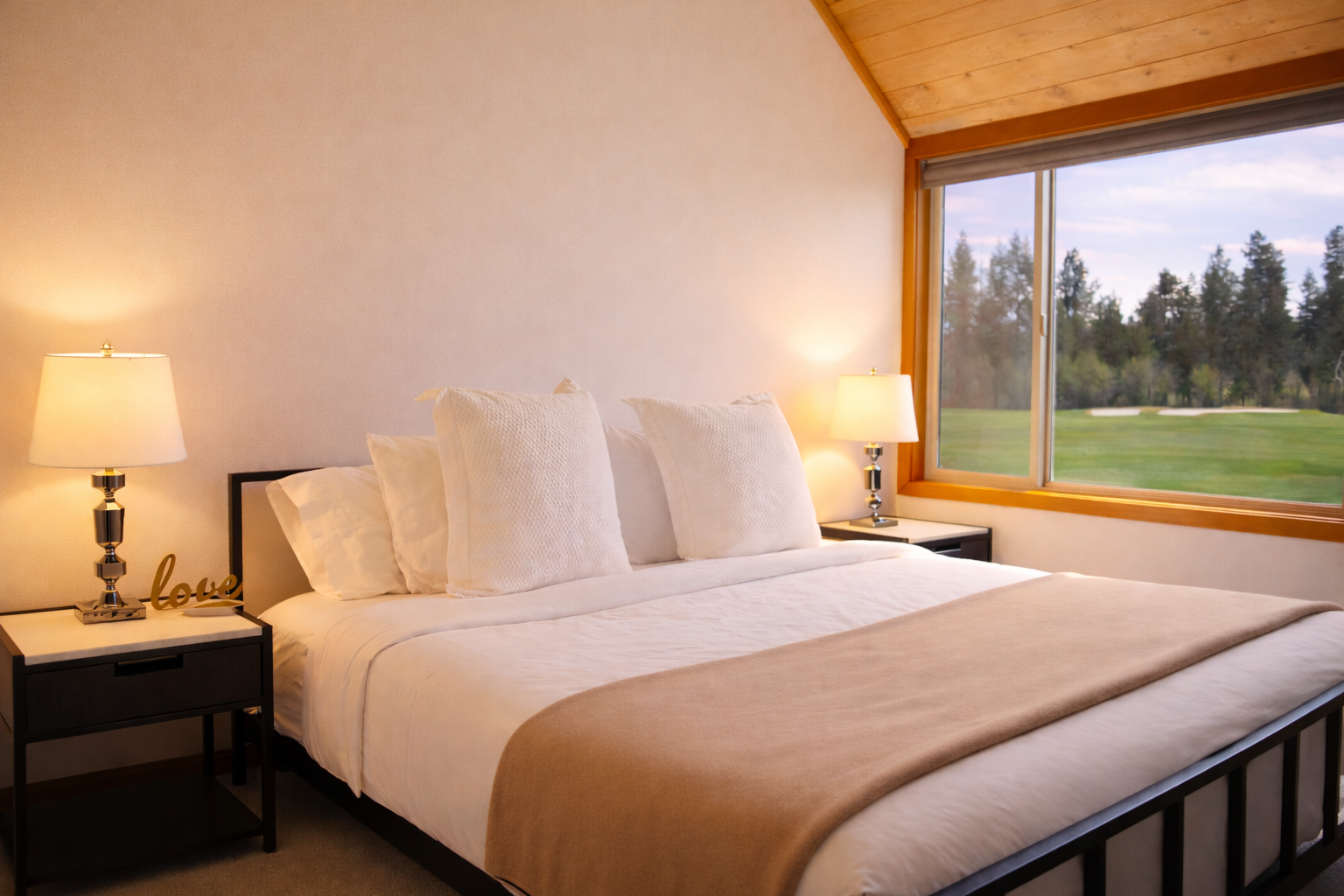 Wake up to stunning golf course views from your cozy bedroom with warm wood ceilings and soft lighting creating the perfect retreat.