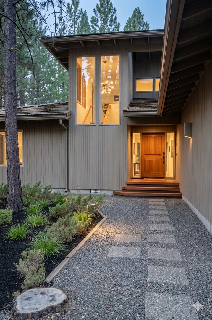 Modern architectural entrance nestled among towering pines features warm wood accents, elegant stone pathway, and contemporary lighting that creates an inviting arrival experience at dusk.