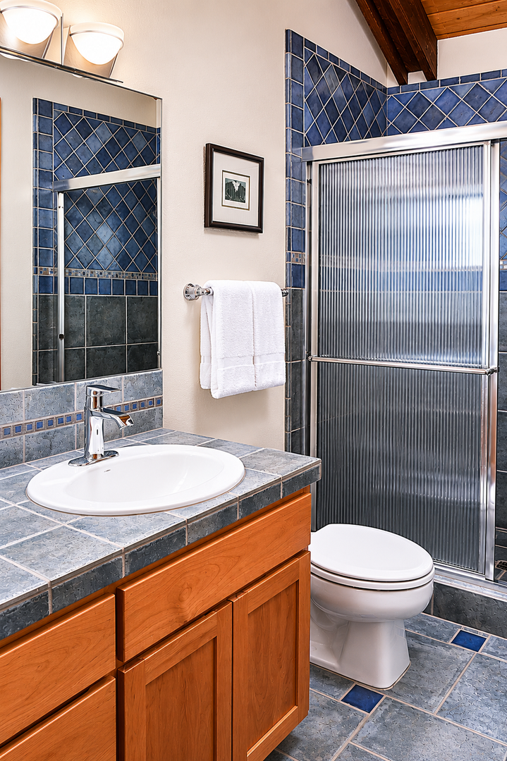 Step into your private bathroom featuring stunning blue diamond-patterned tile, a spacious walk-in shower, and warm wood accents. Fresh towels await your arrival.