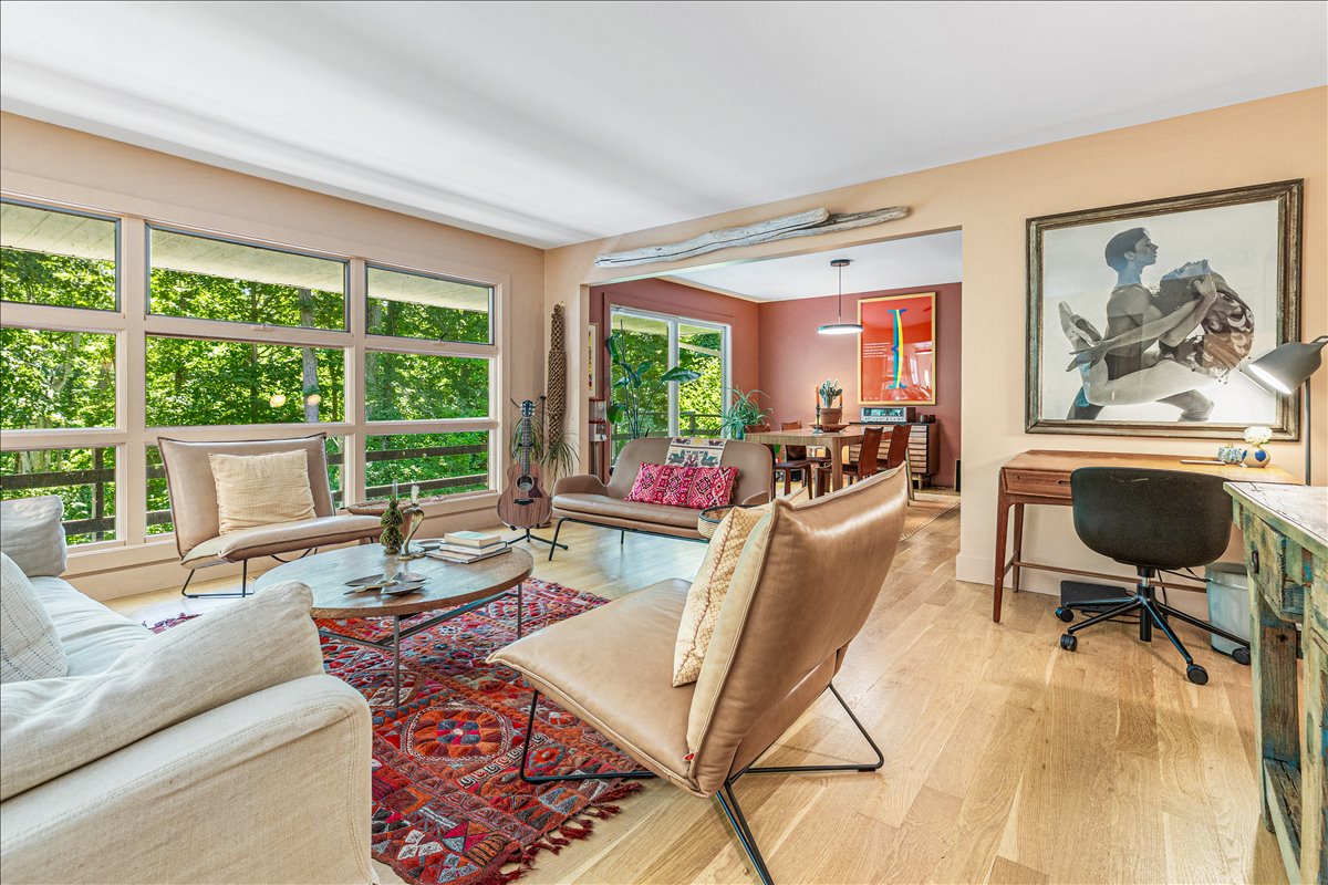 Unwind in your stylish living space featuring leather seating, warm wood floors, and lush garden views through expansive windows.