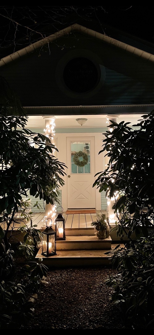 The property entrance glows warmly at night, welcoming guests with softly lit lanterns lining the pathway and lush greenery framing the door.