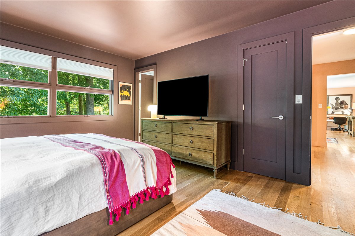 Rest peacefully in your cozy bedroom featuring warm wood floors, a large flat-screen TV, and garden views through sunny windows.