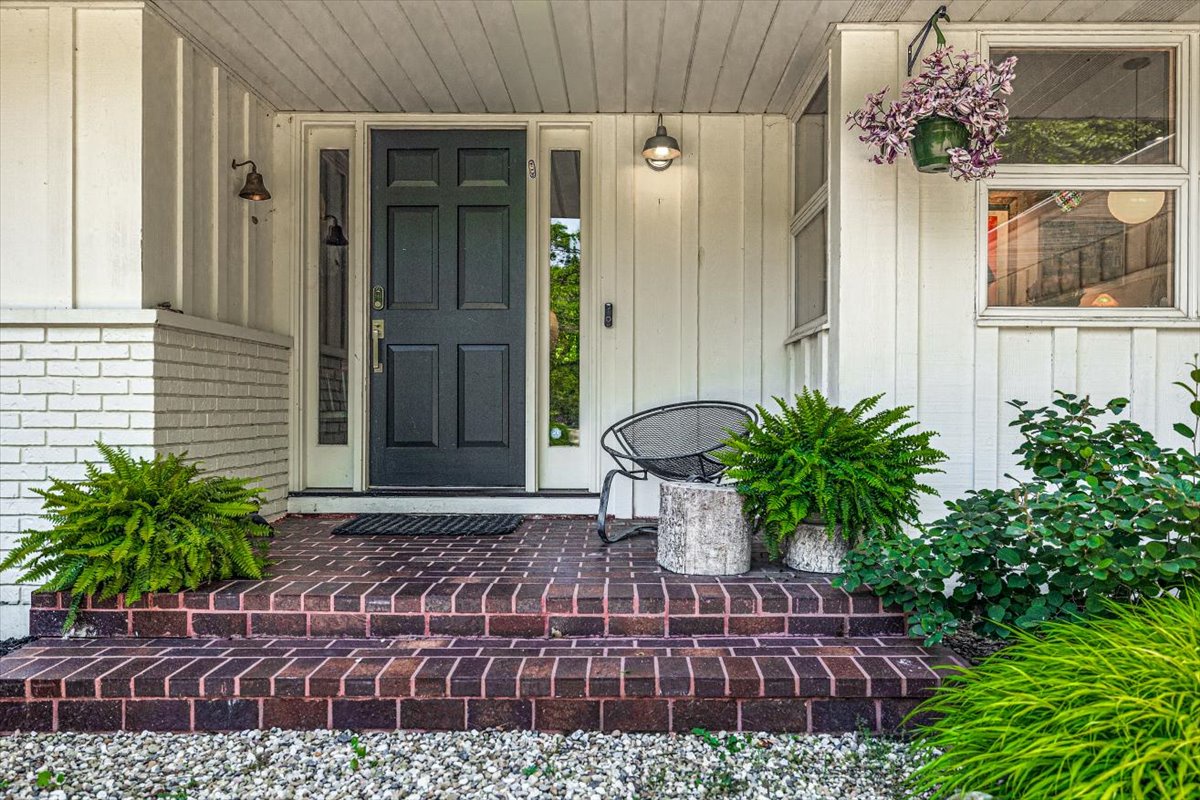 Charming front entrance with welcoming blue door, brick steps, and lush greenery creates an inviting arrival experience.