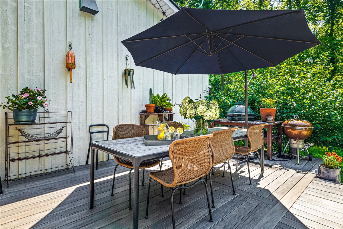 Your private deck offers a perfect outdoor dining space with a charming table, umbrella shade, and BBQ grill surrounded by lush garden views.