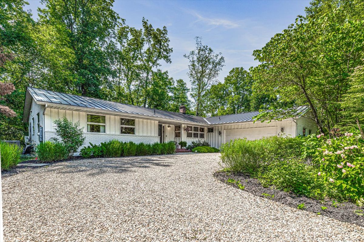 Modern ranch-style home nestled among mature trees with gravel driveway and landscaped gardens creating a peaceful retreat setting.