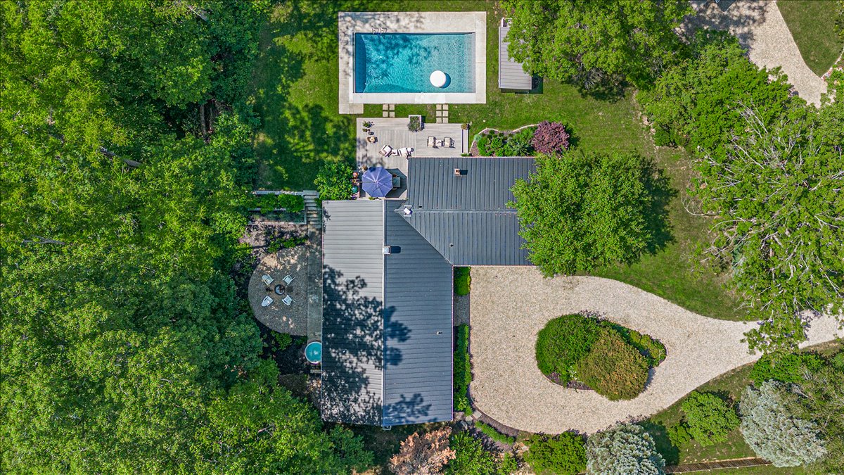 Aerial view of modern property featuring swimming pool, landscaped grounds, and outdoor entertainment areas surrounded by lush natural vegetation.