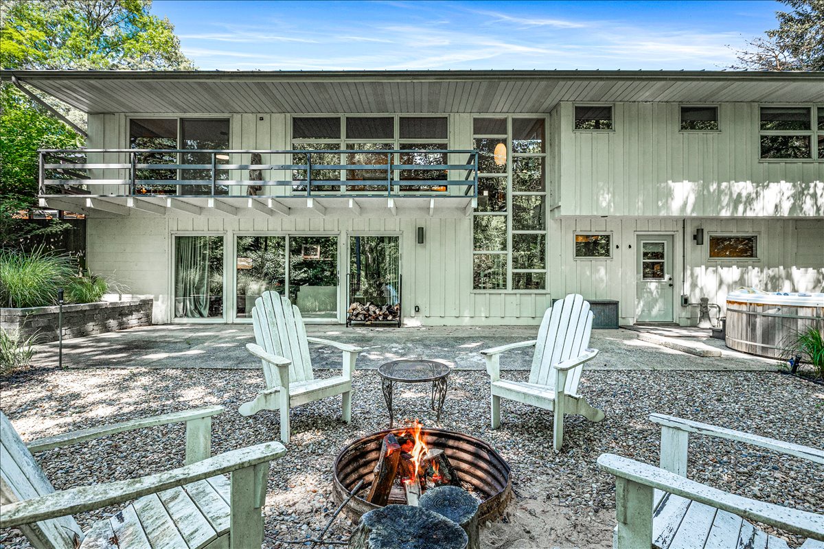 Modern two-story retreat with outdoor fire pit and seating area surrounded by mature trees.