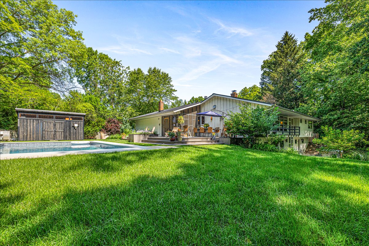 Modern architectural retreat nestled among mature trees with swimming pool and expansive lawn areas.