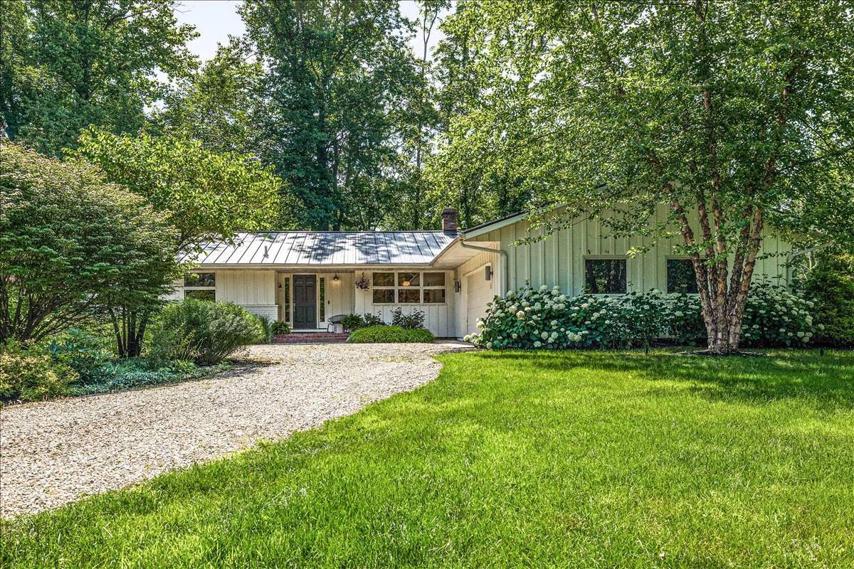 Mid-century modern retreat nestled among mature trees with private gravel drive and manicured lawn for peaceful arrival.