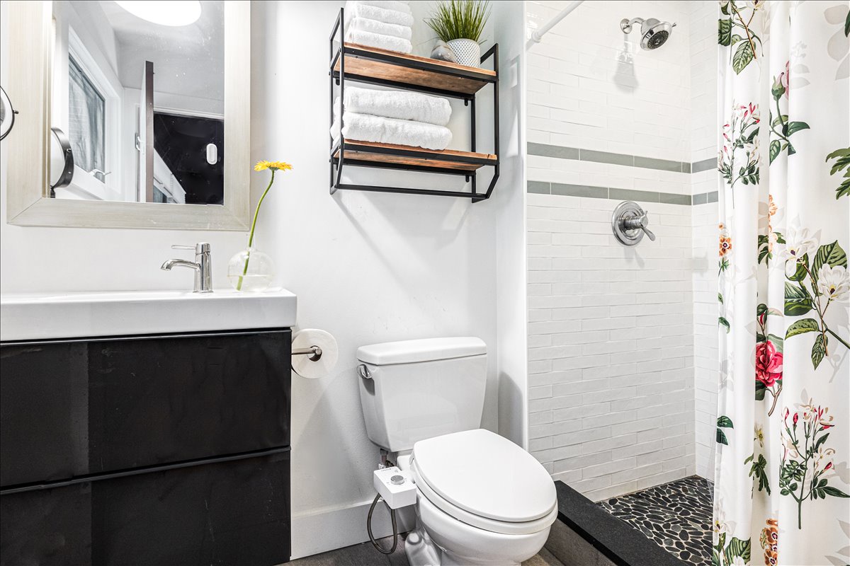 Your stylish bathroom features fresh white subway tiles, a rainfall shower, and thoughtful touches like floating shelves and a cheerful flower accent.