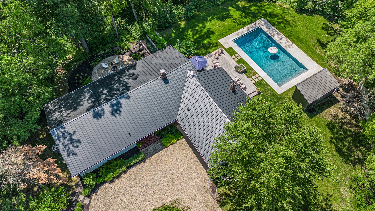 Aerial view of a private estate featuring a sparkling swimming pool surrounded by lush greenery and mature trees.