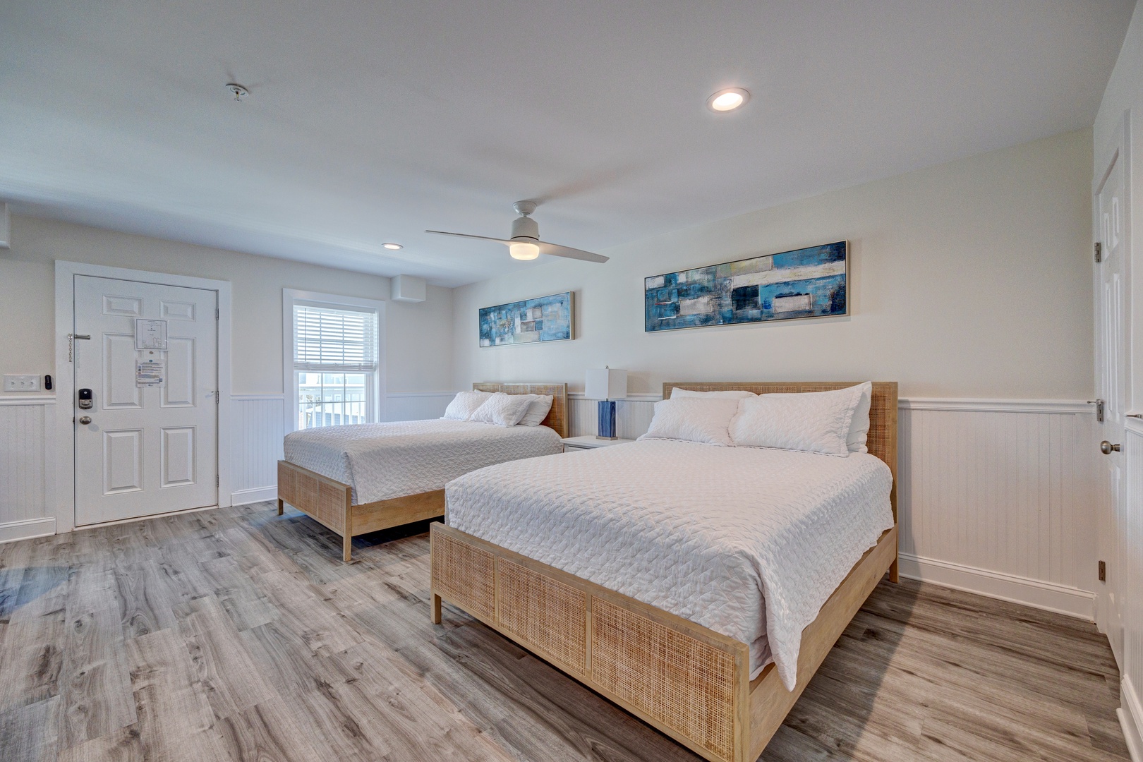 Relax in your spacious bedroom featuring two comfortable beds, coastal artwork, and a cooling ceiling fan for peaceful nights.