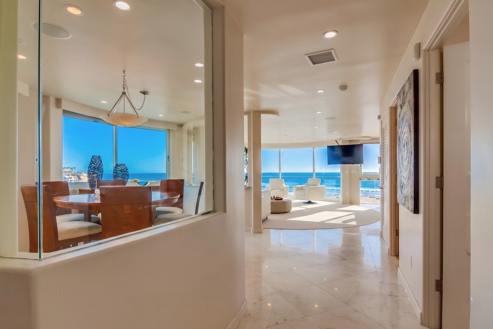 Oceanfront luxury home with floor-to-ceiling windows framing endless blue-water vistas, bright open interiors, and seamless flow from dining to lounge areas.