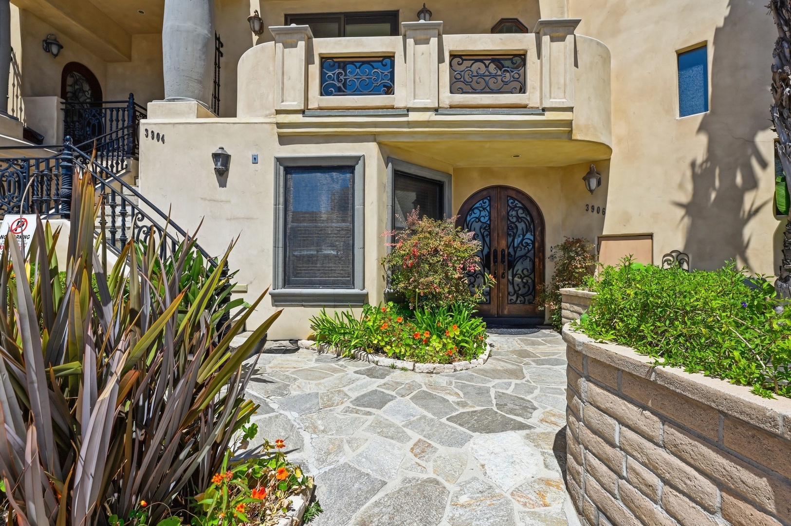 Mediterranean-style building entrance with decorative ironwork, stone pathways, and lush landscaping creates an elegant arrival experience.